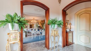 Un amplio pasillo con piso de mármol, puertas de madera decoradas y helechos en macetas.