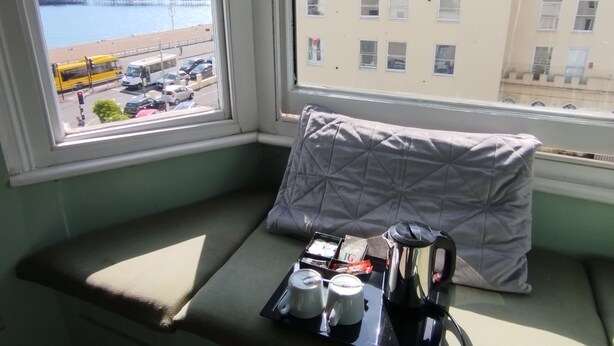 Asiento junto a la ventana en esquina con cojín, bandeja con tetera, tazas y caja de pañuelos.