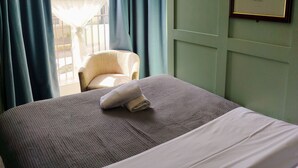 Una cama bien hecha con una almohada blanca y una toalla doblada, una silla y un cuadro en la pared.
