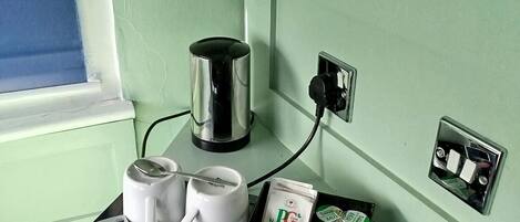 A small kitchenette with a coffee maker, two mugs, a remote control, and a tray of snacks.