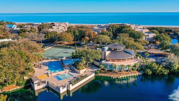 Eine Vogelperspektive eines Resorts mit einem Hauptgebäude, einem Tennisplatz, einem Schwimmbad und einem Gewässer.
