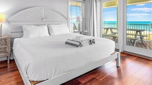 Ein Schlafzimmer mit Bett, Deckenventilator, Nachttisch, Lampe und Blick auf den Strand.