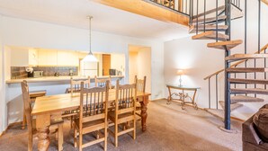 A dining area with a wooden table and chairs, a kitchen in the background, and a spiral staircase. - Perfect Ski-in/out condo Center Village, Free Parking, WiFi, Amazing views (Copper Mountain)