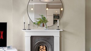 Una sala de estar moderna con chimenea, un espejo redondo encima y una planta en el repisa.