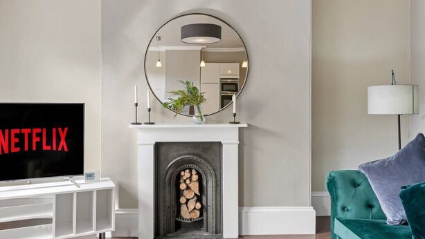 Una sala de estar con chimenea, televisor, un sofá verde y un espejo en la pared.