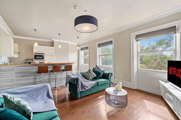 A modern living room with a green sofa, a coffee table, and a TV displaying 'NETFLIX'. - Luxury Yorkshire Apartment 4 - Parking (Wakefield)