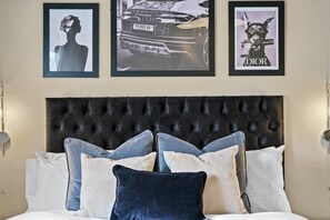 A bedroom with a tufted headboard, a bed with multiple pillows, and three framed pictures on the wall. - Luxury Yorkshire Apartment 4 - Parking (Wakefield)