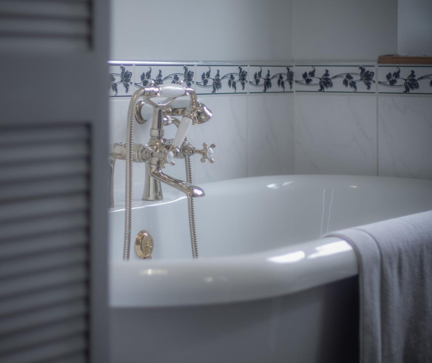 A bathtub with a faucet and shower head, a towel, and a tiled wall with floral patterns.