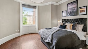 Ein Schlafzimmer mit großem Fenster, einem karottengeknöpften Kopfteil und gerahmten Bildern an der Wand.
