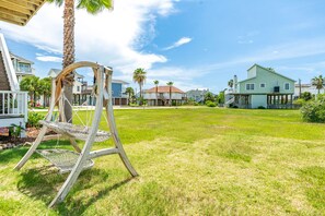 A grassy yard with a swing set, a house with a porch, and a clear blue sky.