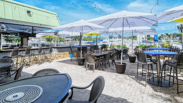 An outdoor patio area with tables and chairs, umbrellas, and a view of the marina.