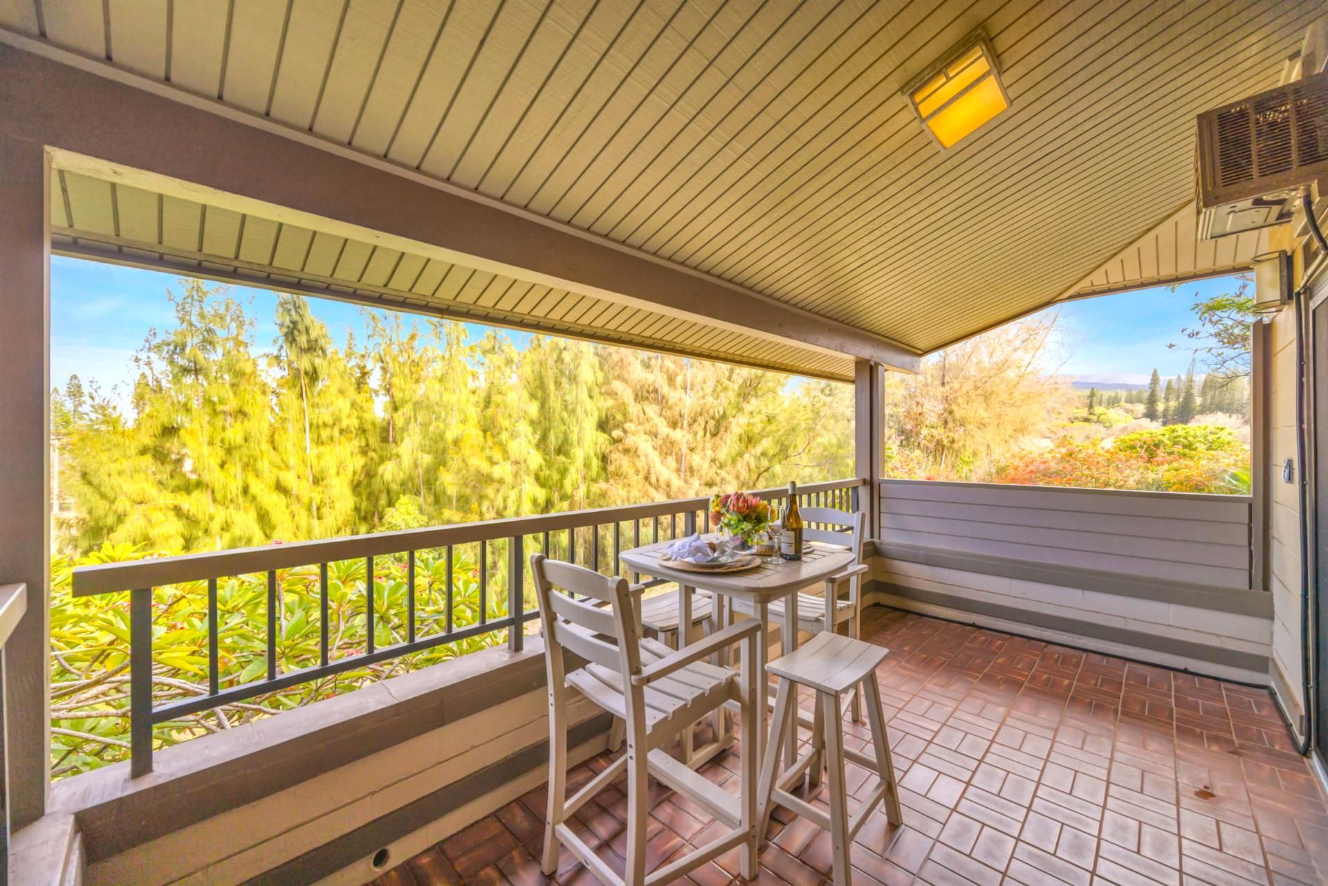 A covered patio with a table and chairs, a railing, and a view of trees and hills.
