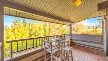 A covered patio with a table and chairs, a railing, and a view of trees and hills.