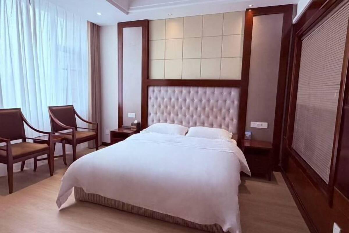 Una habitación de hotel con una cama grande, dos mesitas de noche, una silla y una ventana con cortinas.