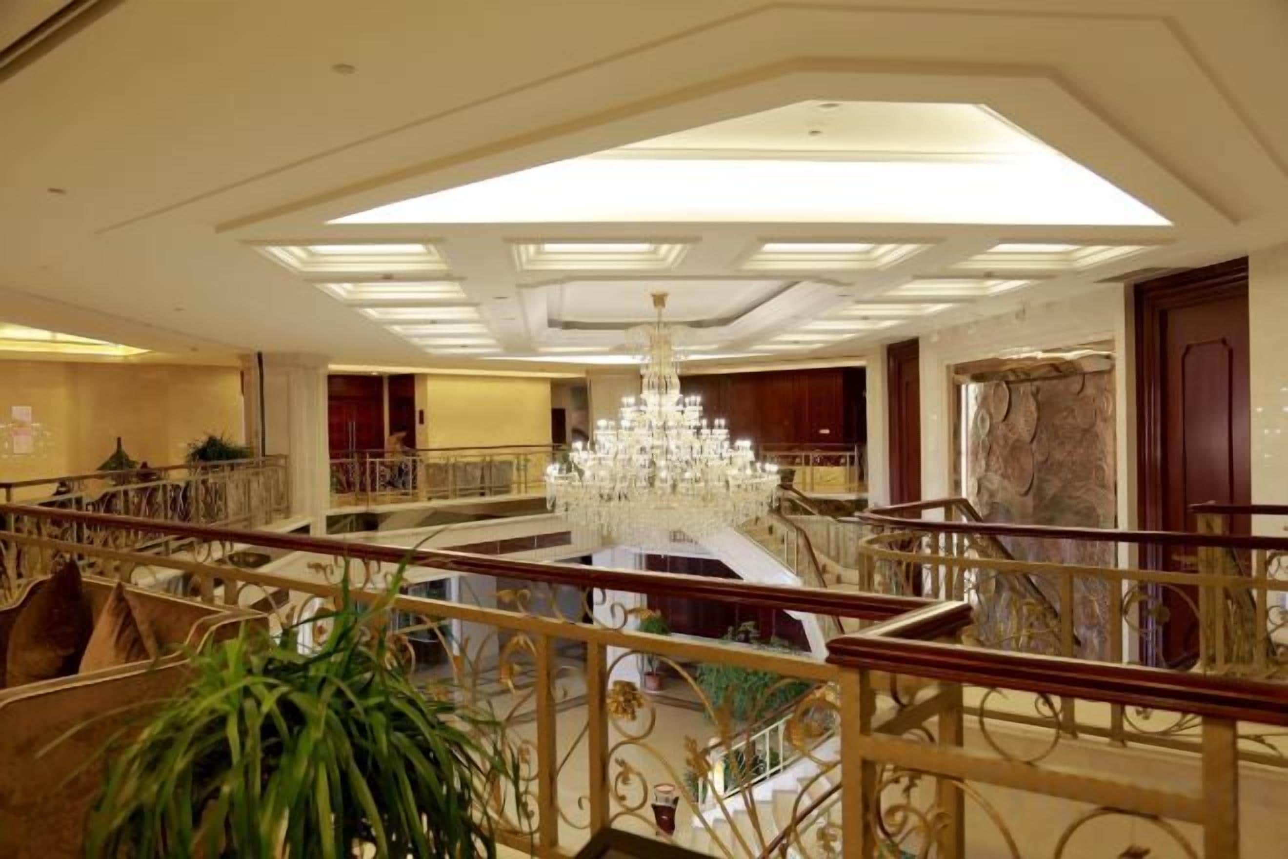 A grand lobby with a central staircase, a chandelier, and a view of the upper floor.