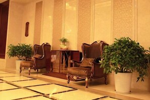 A lobby with two upholstered armchairs, a small table with a potted plant, and a large potted plant.