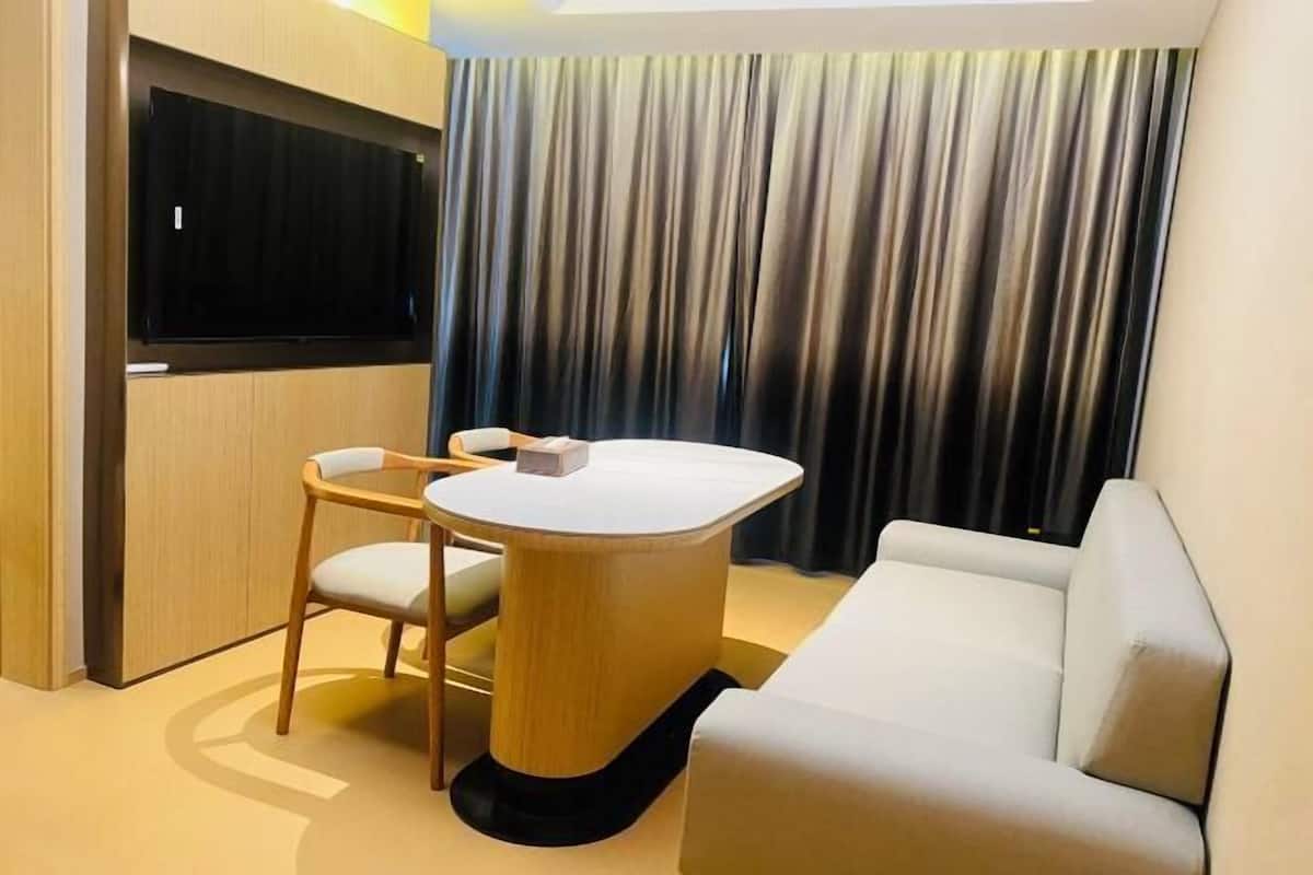 Una habitación de hotel moderna con una mesa redonda, un sofá, un televisor montado en la pared y un fondo de cortina.
