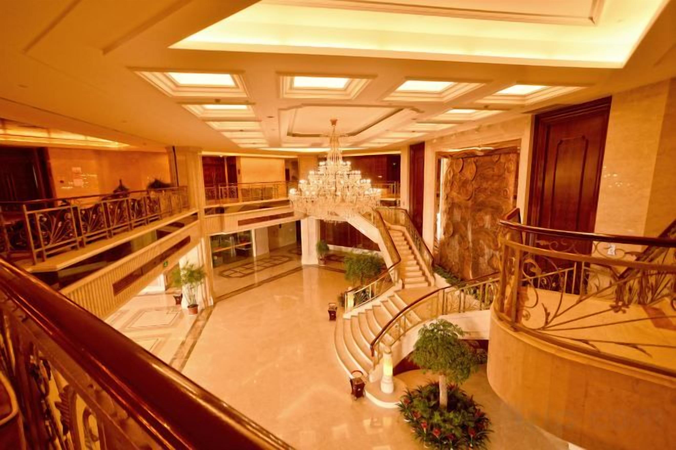 A multi-level hotel lobby with a grand staircase, chandeliers, and a decorative railing.