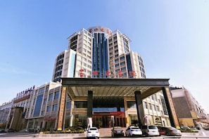 Ein mehrstöckiges Hotel mit markantem Eingang, überdachtem Bereich und mehreren parkenden Autos davor.