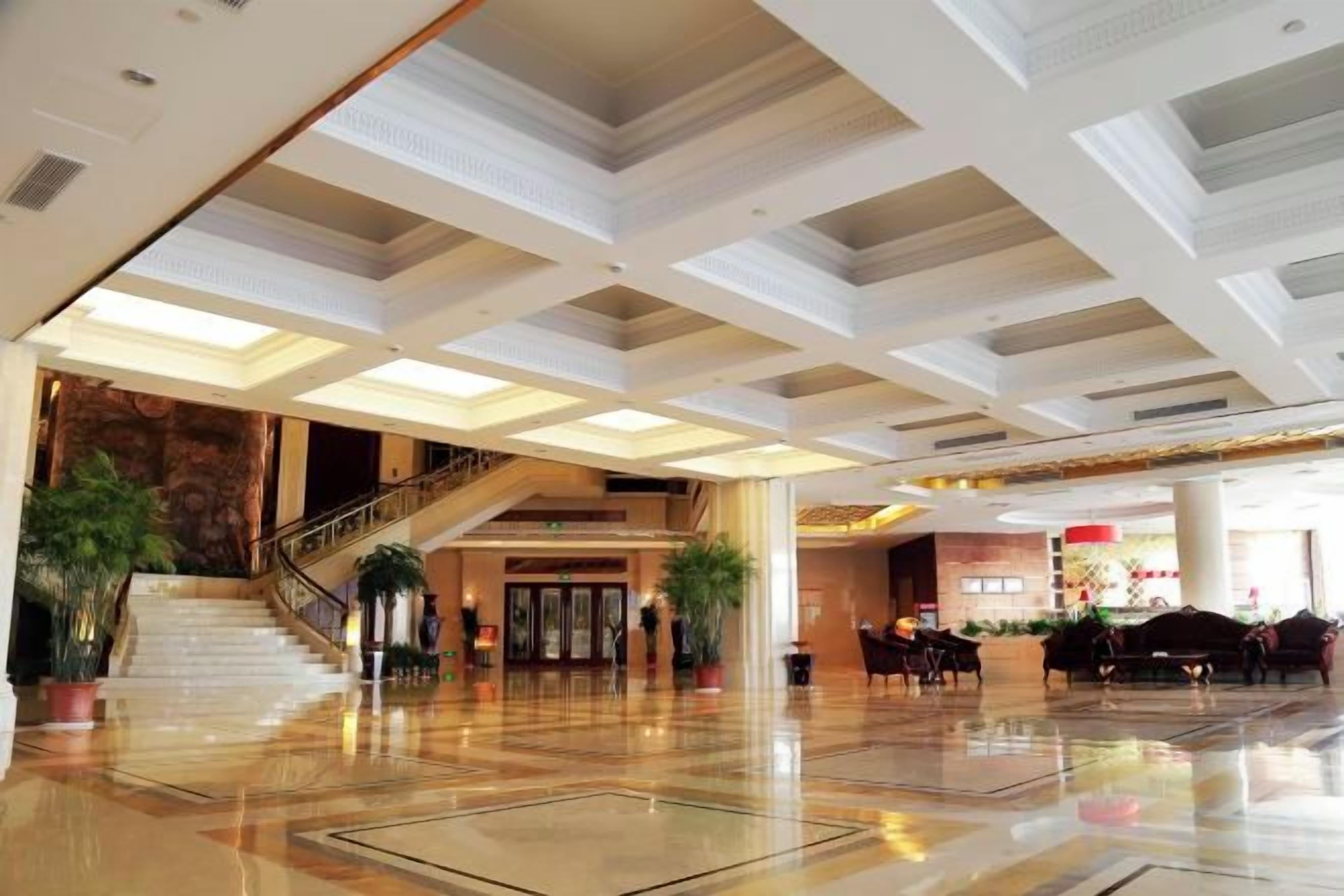 A spacious lobby with a grand staircase, polished floors, and modern lighting fixtures.