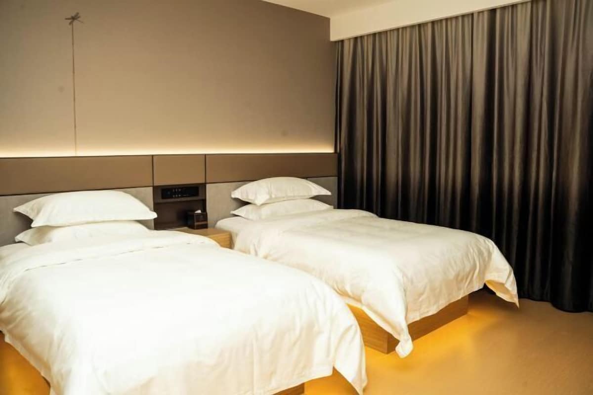 A hotel room with two beds, a headboard with a control panel, and a large curtain.
