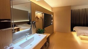 Ein modernes Hotelzimmer mit einem großen Spiegel, einem Waschbecken, einem Bett und einem an der Wand befestigten Flachbildfernseher.