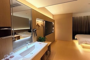 A modern hotel room with a large mirror, a sink, a bed, and a flat-screen TV mounted on the wall.