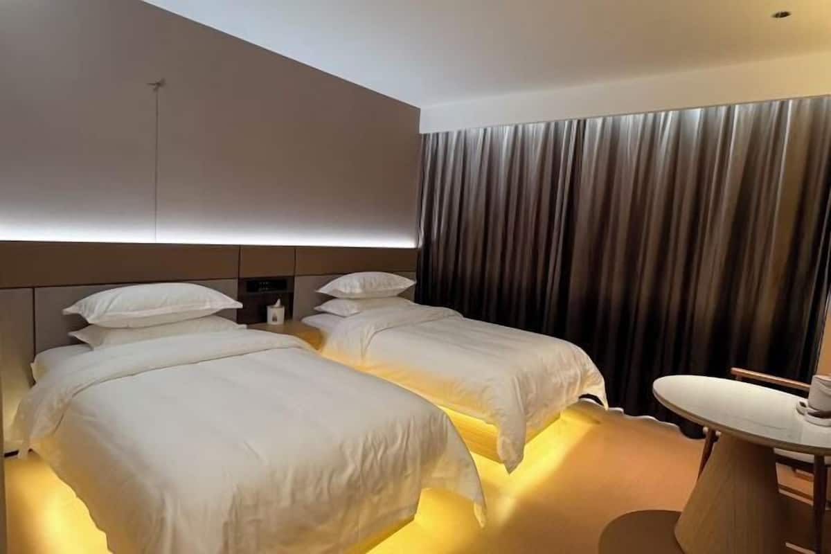 Una habitación de hotel con dos camas, una mesita de noche y un ventanal con cortinas.