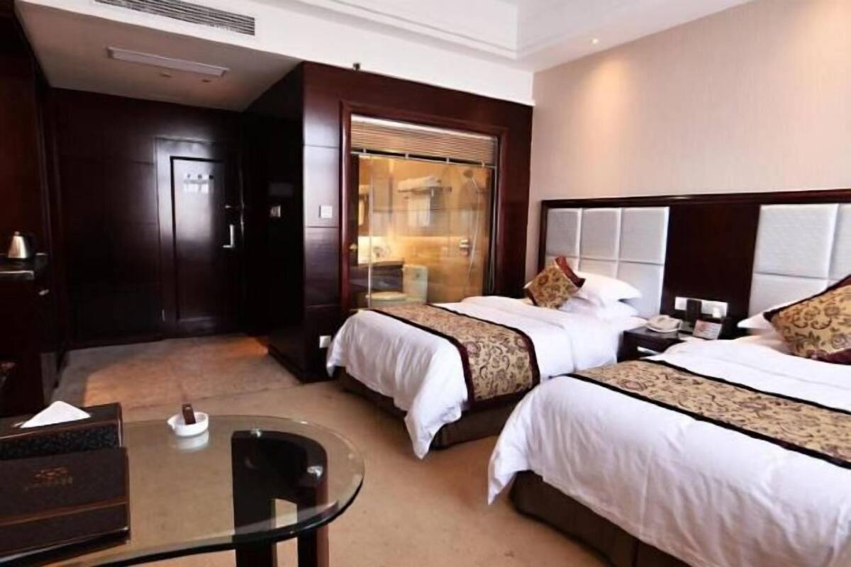 Habitación de hotel con dos camas, una mesa de vidrio, un escritorio y un armario.
