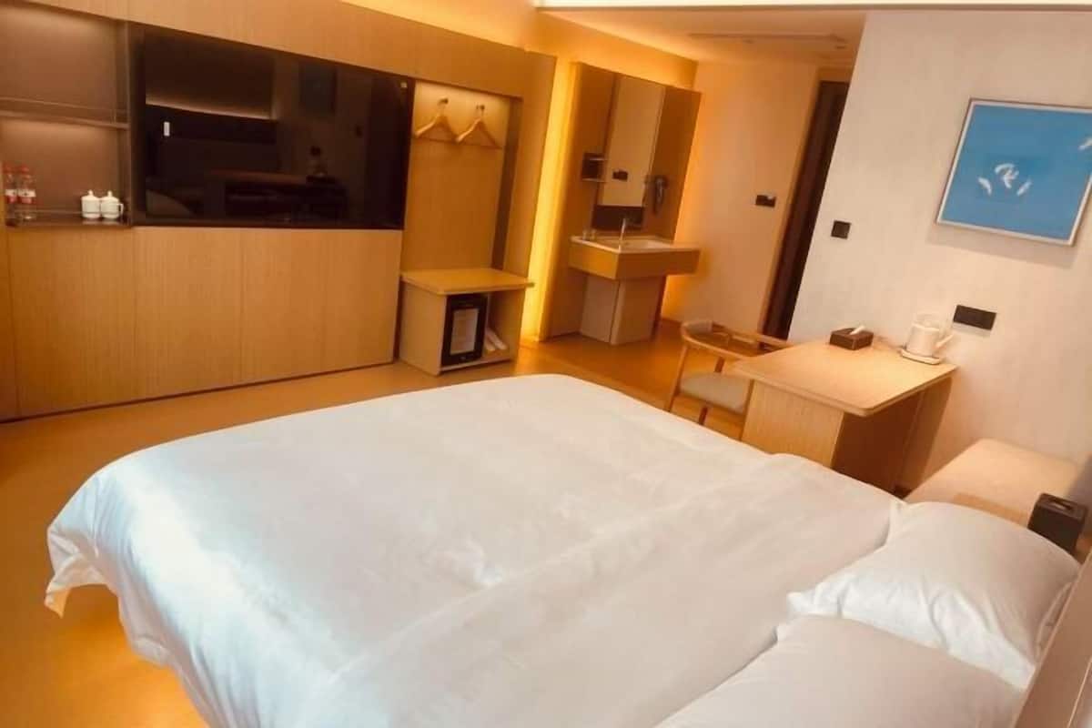 Una habitación de hotel con una cama grande, un escritorio, un espejo y una kitchenette pequeña.