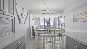 A kitchen with a dining area, featuring a chandelier, white cabinetry, and a view through the window.