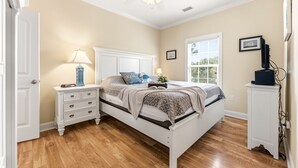 A bedroom with a bed, nightstands, a ceiling fan, a window, and a desk with a computer.