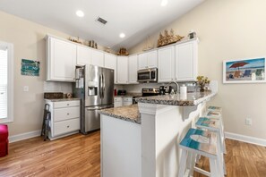 Cocina con armarios blancos, electrodomésticos de acero inoxidable, encimera de granito y una pequeña isla con taburetes.
