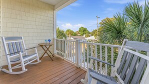 A wooden porch with rocking chairs and a small table, overlooking a garden with palm trees.