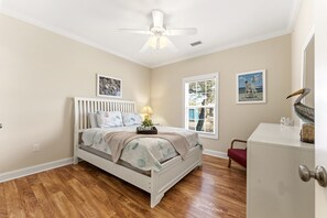 A bedroom with a bed, a ceiling fan, a window with blinds, and a desk.