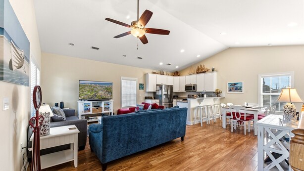 A spacious living room with a blue sofa, a dining area with white furniture, a kitchen with white cabinets, and a ceiling fan.