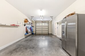 Un garaje con un refrigerador de acero inoxidable grande, una puerta de garaje y diversas herramientas y equipos en estantes.