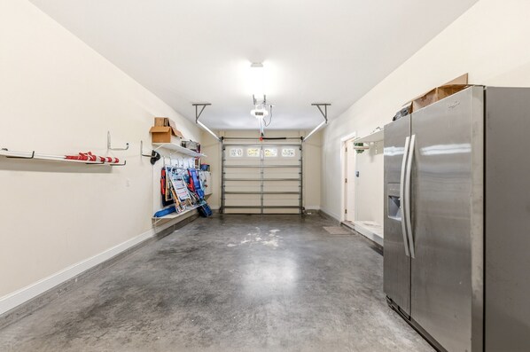 A garage with a large stainless steel refrigerator, a garage door, and various tools and equipment on shelves.