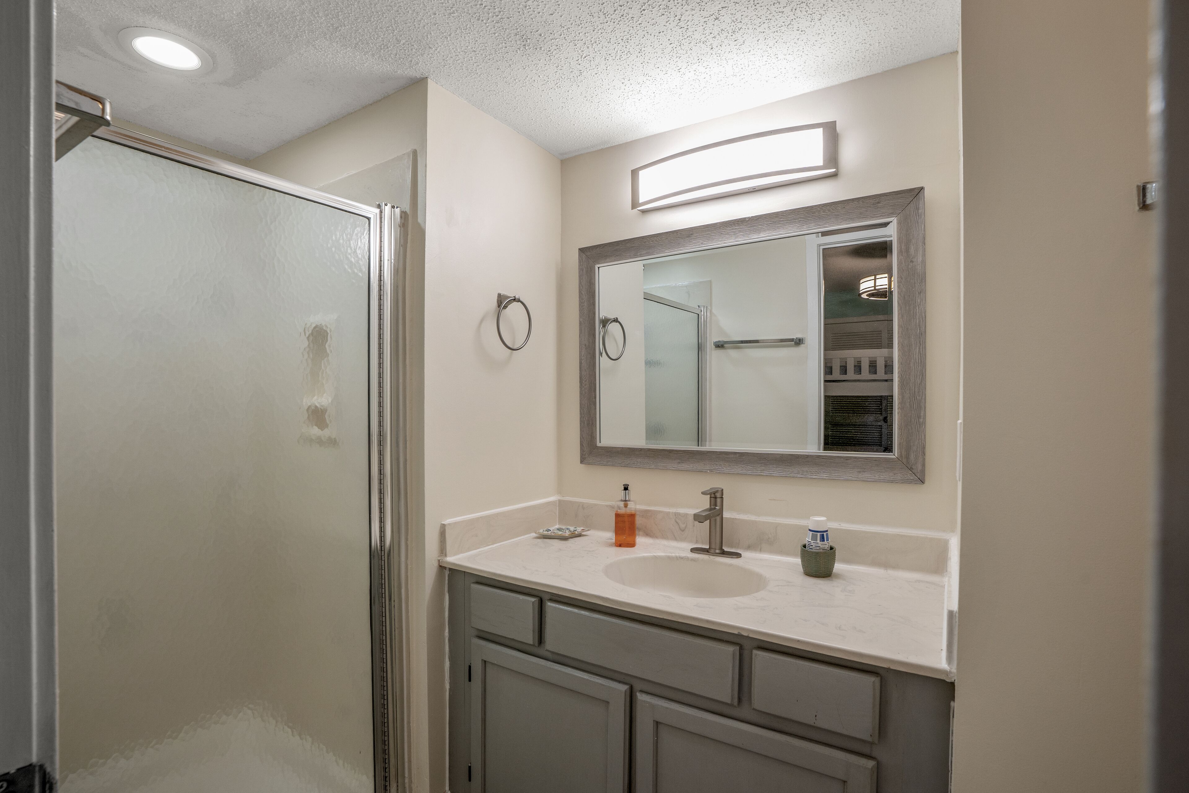 A bathroom with a glass shower enclosure, a sink with a mirror above it, and a vanity with cabinets.