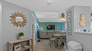 A modern kitchen with a built-in oven, a dining area with a wooden table and chairs, and a living area with a TV and decorative wall art.