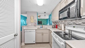 A modern kitchen with a dishwasher, stove, microwave, and a teal backsplash.