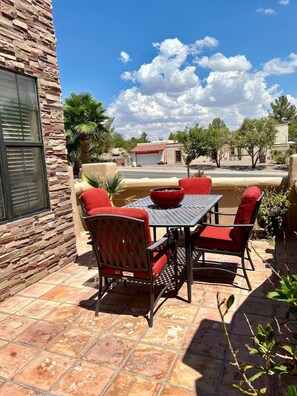 Patio esterno con parete in pietra, tavolo e sedie, e vista su una zona residenziale.