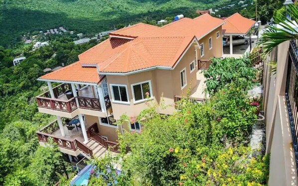 Un immeuble à plusieurs étages, doté d’un toit recouvert de tuiles rouges, de balcons et entouré d’une végétation luxuriante.