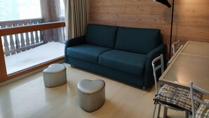 Ett mysigt rum med en blå soffa, två hjärtformade sittpuffar, ett matbord med stolar och en golvlampa.