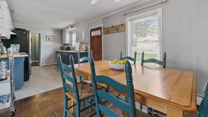 A dining area with a wooden table and teal chairs, a ceiling fan, and a window with blinds. - Bayside Cottage steps from Rock Hall Harbor (Rock Hall)