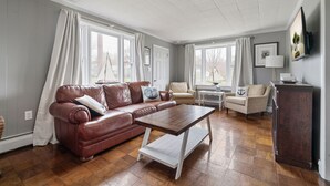 A living room with a brown leather sofa, a wooden coffee table, and two armchairs. - Bayside Cottage steps from Rock Hall Harbor (Rock Hall)