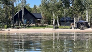 En hytte ved søen med en anløbsbro, omgivet af træer og en sandstrand.