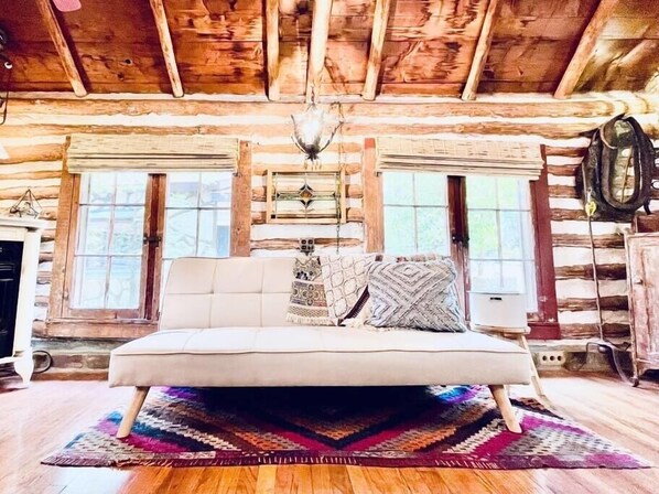 Ein Schlafzimmer in einer Blockhütte mit einem Bett, Fenstern, einer Chandelüstere und einem Teppich.