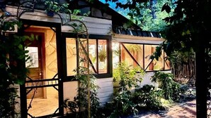 A rustic cabin with a wooden door and large windows, surrounded by lush greenery and a stone pathway. - Downtown Cottage with Private Hot Tub (Eureka Springs)