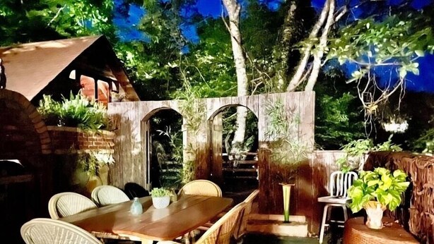 An outdoor patio with a wooden table and wicker chairs, surrounded by greenery and a brick wall. - Downtown Cottage with Private Hot Tub (Eureka Springs)